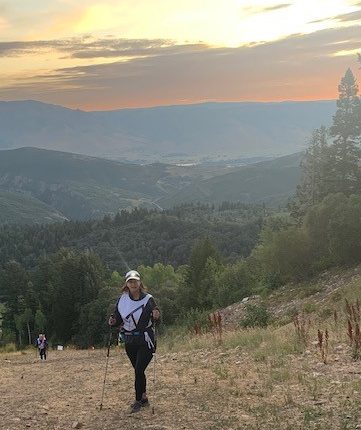 A woman exerts up a hill at sunset or sunrise.